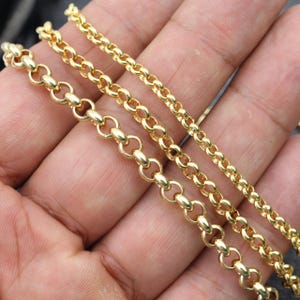 May include: Three gold chains of different thicknesses, displayed on a hand. The chains are made of small, round links.