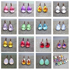 Puede incluir: Surtido de pendientes de cristal en forma de lágrima en varios colores, incluyendo rosa, morado, verde, azul, amarillo, rojo, naranja y transparente. Los pendientes se muestran sobre un fondo gris.