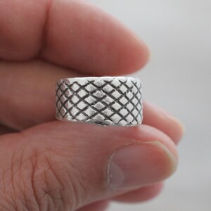 May include: A silver ring with a textured diamond pattern.