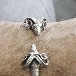 May include: A silver bracelet with two ram head charms. The ram heads are detailed with horns and faces.
