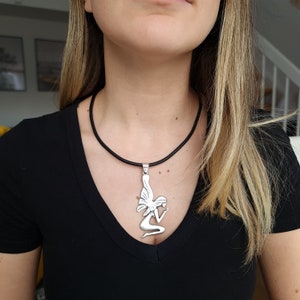 May include: A silver pendant necklace featuring a detailed silhouette of a kneeling fairy with wings. The necklace is on a black leather cord.