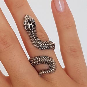 May include: A silver snake ring with a detailed design. The snake is coiled around the finger and has a black flower design on its head.