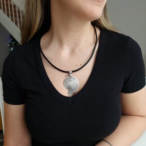 Op de afbeelding: Een zilveren ketting met een spiraalvormige hanger aan een zwart leren koord.