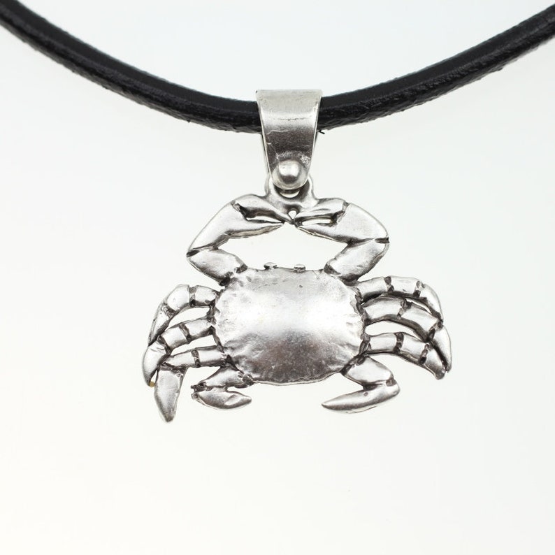 May include: A silver crab pendant necklace with a black leather cord.