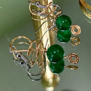 May include: A pair of gold and silver earrings with green gemstone beads. The earrings feature a spiral design and a hook closure.