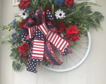 Patriotic Bicycle Wheel Door Wreath with plenty of red, white, and blue flowers ribbons, on greenery sprigs. USA, America , door decor.