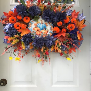 May include: A fall-themed wreath featuring blue and orange flowers, orange pumpkins, and a blue and white pumpkin design in the centre.
