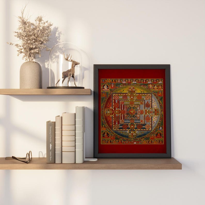Op de afbeelding: Een ingelijste print van een kleurrijke mandala met ingewikkelde details. De mandala is geplaatst tegen een rode achtergrond en omgeven door een zwarte lijst. De print wordt tentoongesteld op een plank met boeken en een decoratief hertenbeeldje.