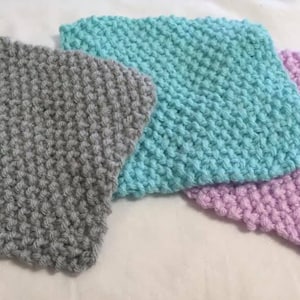 Può includere: Tre quadrati a maglia in diversi colori: grigio, azzurro e lilla chiaro. I quadrati sono realizzati con una maglia testurizzata che conferisce loro un aspetto irregolare.