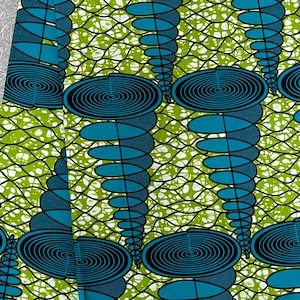 May include: Green and blue fabric with a repeating pattern of circles and ovals. The fabric has a white background with a green and white net pattern. The text "PRINTS SUPER AVOGAN WAX" is printed on the bottom of the fabric.