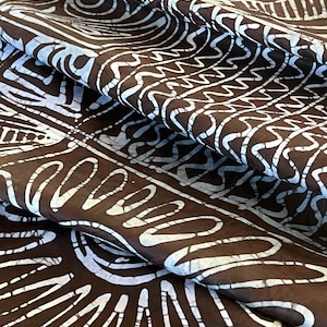 Puede incluir: Tela marr&oacute;n con un patr&oacute;n batik blanco de formas geom&eacute;tricas y l&iacute;neas onduladas. La tela est&aacute; doblada y drapeada, mostrando el patr&oacute;n desde diferentes &aacute;ngulos.