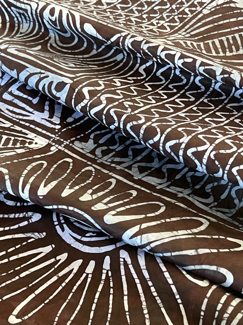 Puede incluir: Tela marr&oacute;n con un patr&oacute;n batik blanco de formas geom&eacute;tricas y l&iacute;neas onduladas. La tela est&aacute; doblada y drapeada, mostrando el patr&oacute;n desde diferentes &aacute;ngulos.