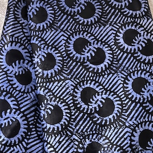 Puede incluir: Tela azul y negra con un patrón repetitivo de soles estilizados. Los soles son negros con un contorno blanco y están rodeados de un patrón azul y blanco.
