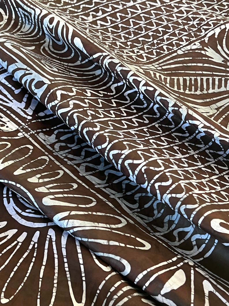 Puede incluir: Tela marr&oacute;n con un patr&oacute;n batik blanco. El patr&oacute;n presenta una variedad de formas geom&eacute;tricas, incluyendo c&iacute;rculos, cuadrados y tri&aacute;ngulos.