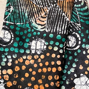 May include: Black fabric with a batik design featuring white, orange, and teal colours. The fabric has a pattern of circles and lines.