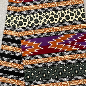 May include: A colorful fabric with a repeating pattern of black and white geometric shapes, brown and orange zebra stripes, and black and white leopard spots. The fabric is folded in half and the text "ABUNDANT" is visible in the lower left corner.