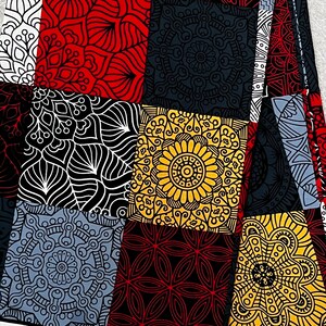 May include: A fabric with a patchwork design featuring various geometric and floral patterns in red, black, white, yellow, and gray. The fabric is folded, revealing the intricate details of each square.