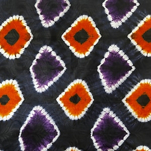 Puede incluir: Una tela negra con un patrón repetitivo de diseños de tie-dye en forma de diamante. Los diamantes son en tonos de naranja, morado, blanco y negro.