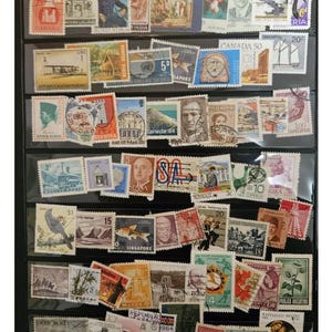 Könnte beinhalten: Eine Sammlung farbenfroher Briefmarken aus verschiedenen Ländern, ausgestellt in einem schwarzen Album. Die Briefmarken zeigen vielfältige Bilder, darunter Porträts, Gebäude und Naturszenen. Einige Briefmarken tragen Texte wie "CANADA" und "SINGAPORE".
