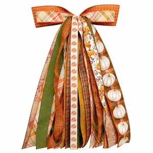May include: A decorative bow made of multiple ribbons in autumn colors including orange, green, and tan. The ribbons feature patterns of plaid, solid textures, and a print of white pumpkins, orange pumpkins, and autumn leaves on a cream background.