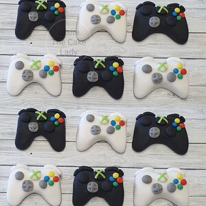 May include: Twelve edible cake toppers shaped like video game controllers. Six are black with green and coloured buttons, and six are white with green and coloured buttons.