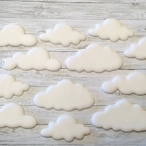 May include: A collection of 13 white fondant clouds, ideal for decorating cakes or cupcakes. The clouds are various sizes and shapes, with some having a more rounded shape and others having a more irregular shape.