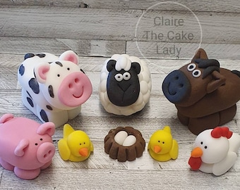 Pode incluir: Uma coleção de figuras de animais de fazenda, incluindo uma vaca com manchas pretas, uma ovelha, um cavalo, um porco rosa, dois pintinhos amarelos, um ninho com ovos e uma galinha branca com crista vermelha. As figuras são provavelmente feitas de pasta de açúcar ou argila.