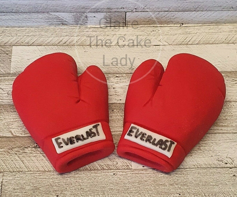 May include: Two red boxing gloves with white Everlast branding. The gloves are made of fondant and are perfect for a boxing themed cake.