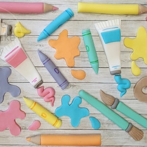 May include: A set of fondant art supplies for a cake topper. The set includes paint tubes, paintbrushes, crayons, pencils, and paint splatters in various colours.