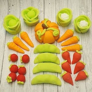 May include: Assortment of green and orange fondant decorations, including a pumpkin, pea pods, and flowers. There are also red and orange fondant decorations shaped like strawberries and carrots.