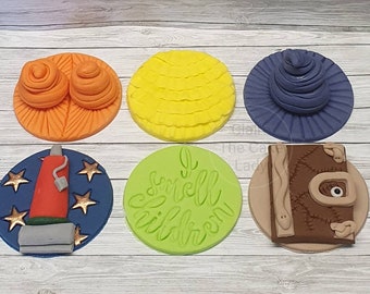 May include: Six round edible cake toppers with various designs. The toppers feature a yellow ball of yarn, a purple wizard hat, a brown book with a snake and an eye, a red vacuum cleaner on a blue background with gold stars, two orange balls of yarn on an orange background, and a green circle with the text "I smell children".
