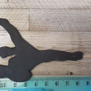 May include: Black silhouette of a narwhal, a type of whale with a long, spiraled tusk, on a wooden background. The silhouette is about 8 inches long.