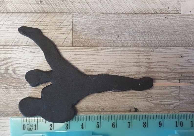 May include: Black silhouette of a narwhal, a type of whale with a long, spiraled tusk, on a wooden background. The silhouette is about 8 inches long.