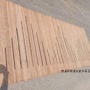 May include: A natural fiber rug with a striped pattern in beige and black. The rug has a subtle texture and is made of natural materials.