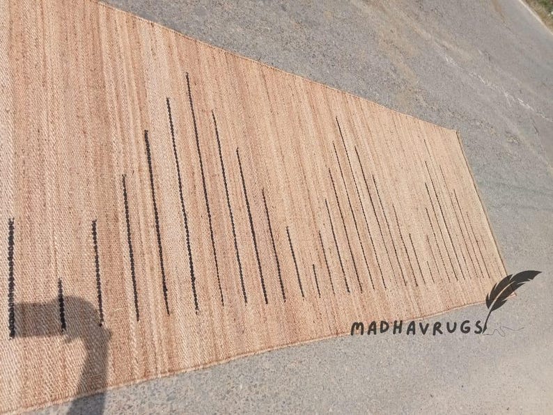 May include: A natural fiber rug with a striped pattern in beige and black. The rug has a subtle texture and is made of natural materials.