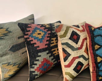 May include: Four decorative throw pillows with geometric patterns in shades of blue, green, red, yellow, and black. The pillows are made of woven fabric and have a rustic, bohemian style.