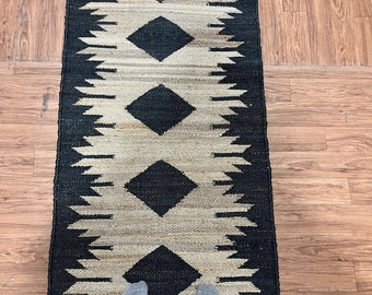 May include: Black and white geometric patterned rug with a diamond design. The rug is made of natural fibers and has a rustic look.