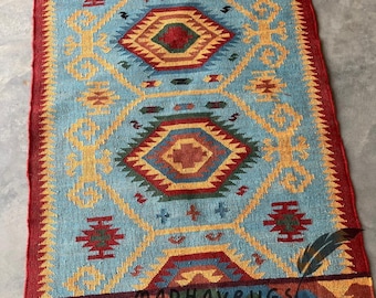May include: A blue, red, yellow, and green patterned rug with fringe. The rug has a geometric design and is made of wool.