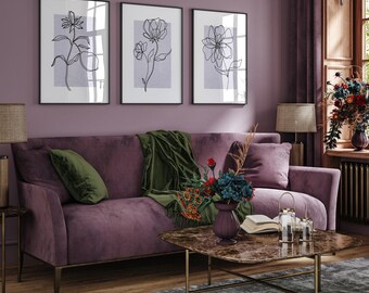 Op de afbeelding: Een pluche paarse fluwelen bank met een groene deken en een marmeren salontafel in een woonkamer met drie zwarte ingelijste lijntekeningen van bloemen op een paarse muur.