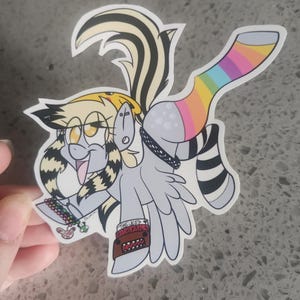 May include: A cartoon sticker of a grey winged pony with yellow and black striped hair, wearing a rainbow striped sock, a black and white striped sock, a black choker with a silver charm, and a brown wristband with the text "THE USED" and "ALL THAT I'VE GOT".