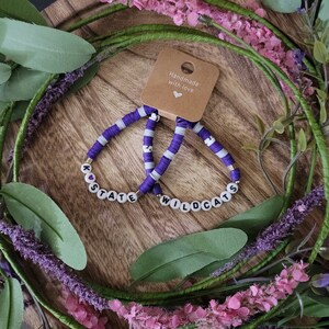 May include: Two purple and white beaded bracelets with the words "K-State Wildcats" spelled out in black letters on white beads.