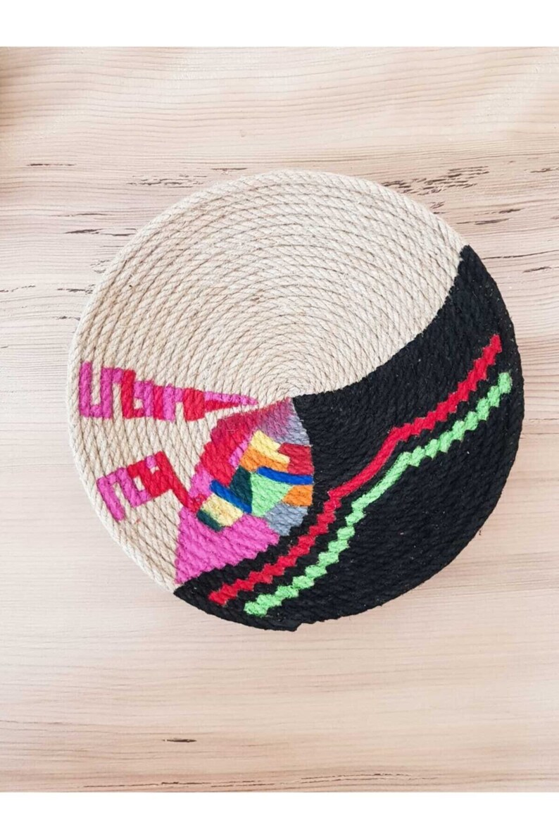 May include: A round woven wall hanging with a black, white, pink, red, green, blue, and yellow geometric design.