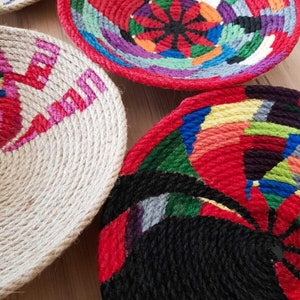 May include: Four round woven baskets with colorful geometric patterns. The baskets are made of natural rope and are decorated with bright colors, including red, blue, green, yellow, and black.
