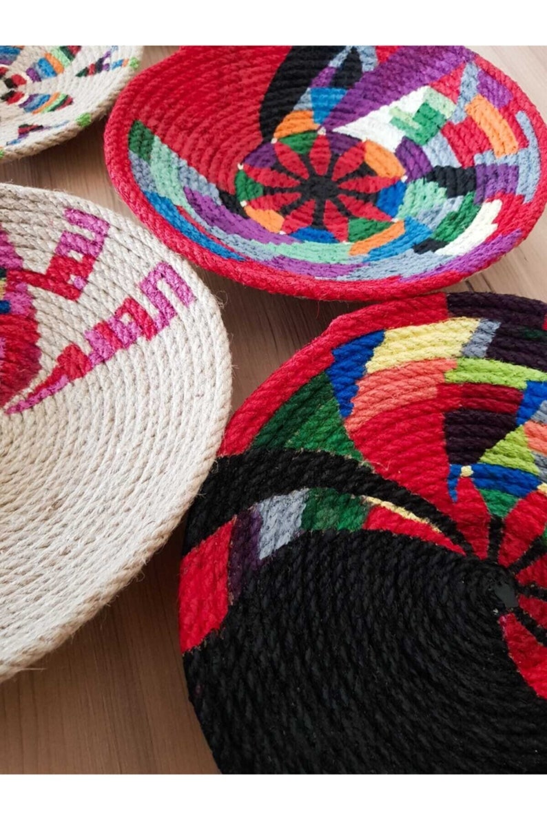 May include: Four round woven baskets with colorful geometric patterns. The baskets are made of natural rope and are decorated with bright colors, including red, blue, green, yellow, and black.