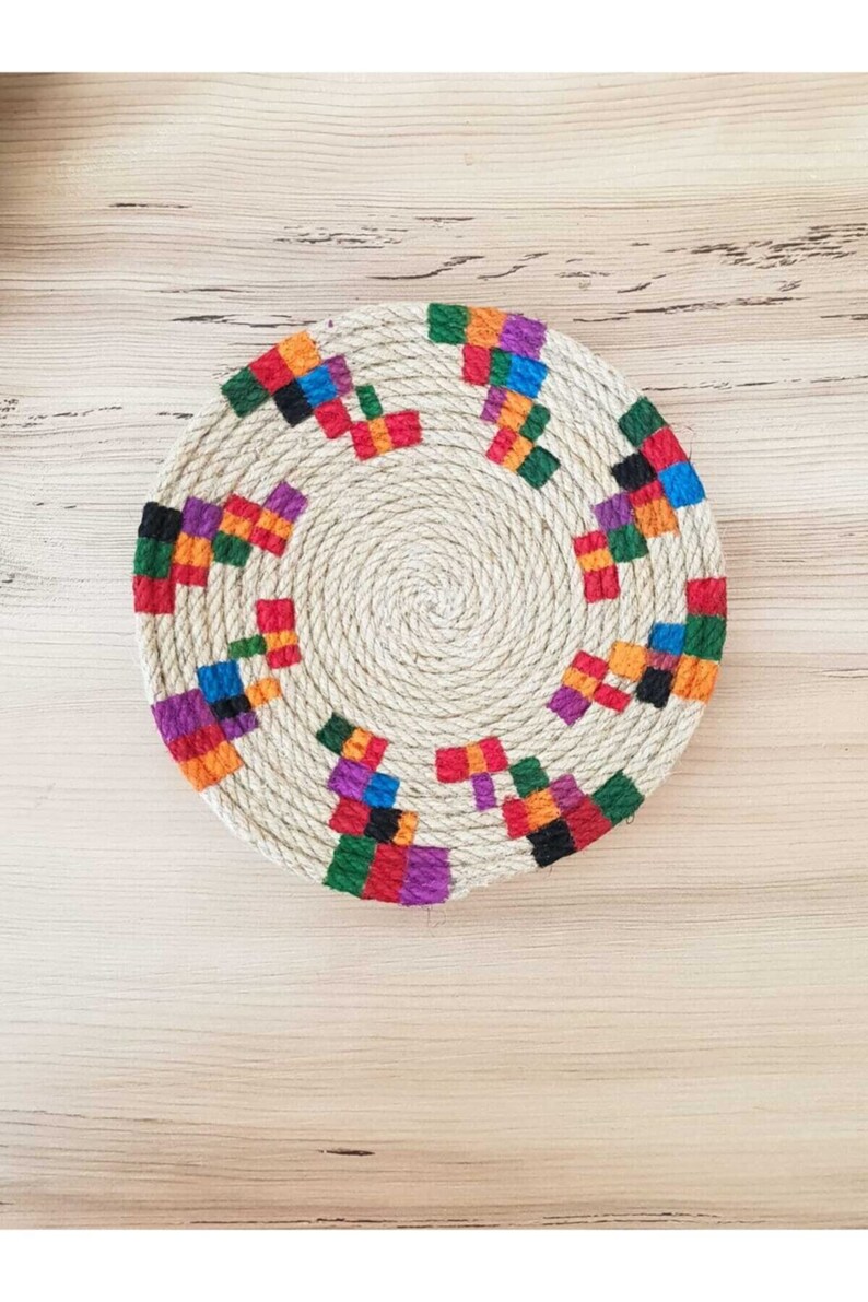 May include: A round, woven coaster with a colorful geometric pattern. The coaster is made of natural fibers and has a rustic, handmade look.