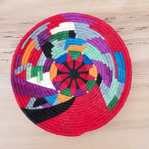 May include: A colorful woven wall hanging with a red background and a geometric pattern in shades of purple, blue, green, orange, and white.