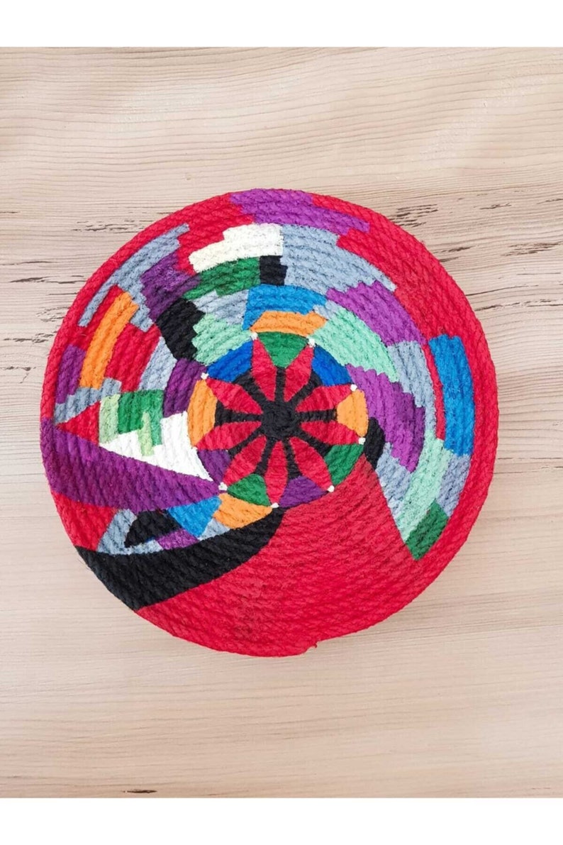 May include: A colorful woven wall hanging with a red background and a geometric pattern in shades of purple, blue, green, orange, and white.