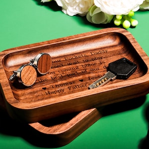 May include: A wooden tray with a personalised message that reads "our Pockets, Daddy can't wait to play you coming home is the best part of our day Thomas Jessi Happy Father's". The tray is filled with cufflinks, a key, and a watch.