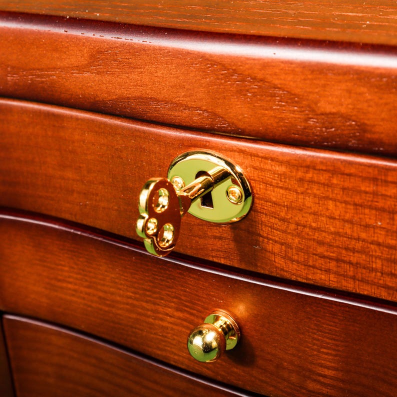 May include: A wooden jewelry box with multiple drawers, featuring a gold-toned keyhole and a decorative knob. The box is made of rich, dark wood with a smooth finish.