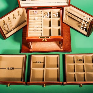 May include: A wooden jewelry box with three drawers. The top drawer has a mirror and compartments for rings and earrings. The bottom two drawers have compartments for necklaces and bracelets. The drawers are labeled with measurements in centimeters: 14.5 cm, 7.0 cm, and 4.5 cm.